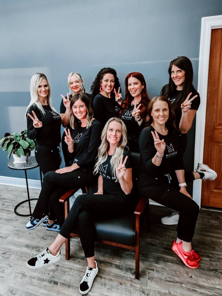 Brittany Perez, Katie Reber, and the rest of the team at MELA Medical Spa and Method Aesthetics Academy in Pensacola, pose for a group photo with peace signs.