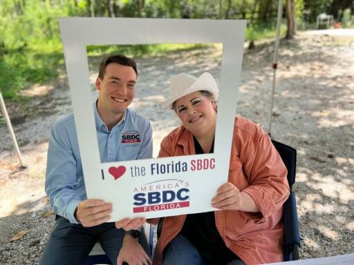 SBDC's Colton Currier and Hammock Bay Soap owner Anita Lesko hold up a sign that says "I (heart) the Florida SBDC Network."
